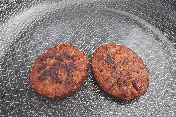 Two cooked burger patties with grill marks are resting in a patterned frying pan.