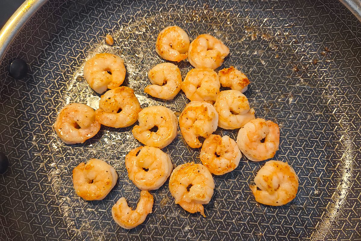Several cooked shrimp pieces are scattered across the surface of a nonstick frying pan with a patterned base.