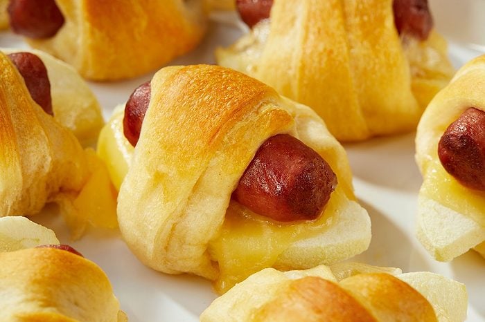 Eye Level horizontal image of golden-brown apple-Gouda pigs in a blanket. The baked crescent rolls encase miniature smoked sausages, melted Gouda cheese, and thin apple slices.
