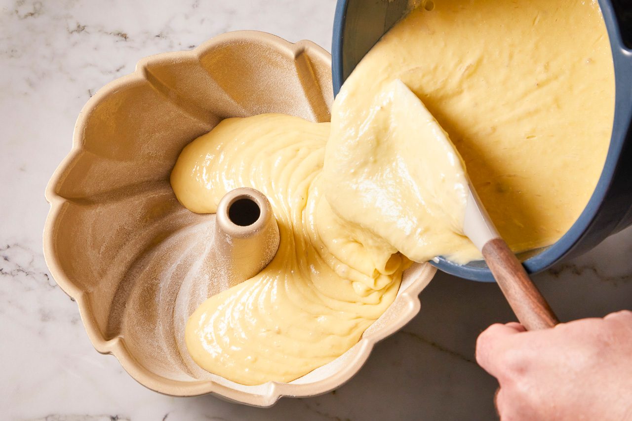 cake batter being poured into a greased and floured 10-inch fluted tube pan