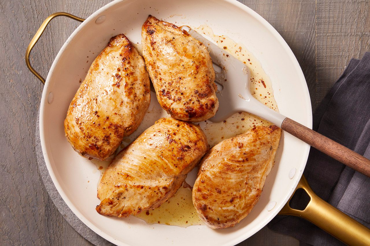 Overhead shot of seasoned chicken breasts seared until golden brown in a white skillet.