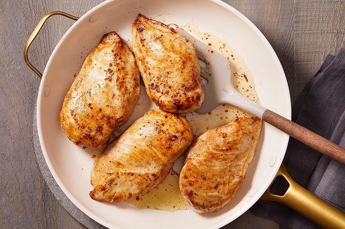Overhead shot of seasoned chicken breasts seared until golden brown in a white skillet.
