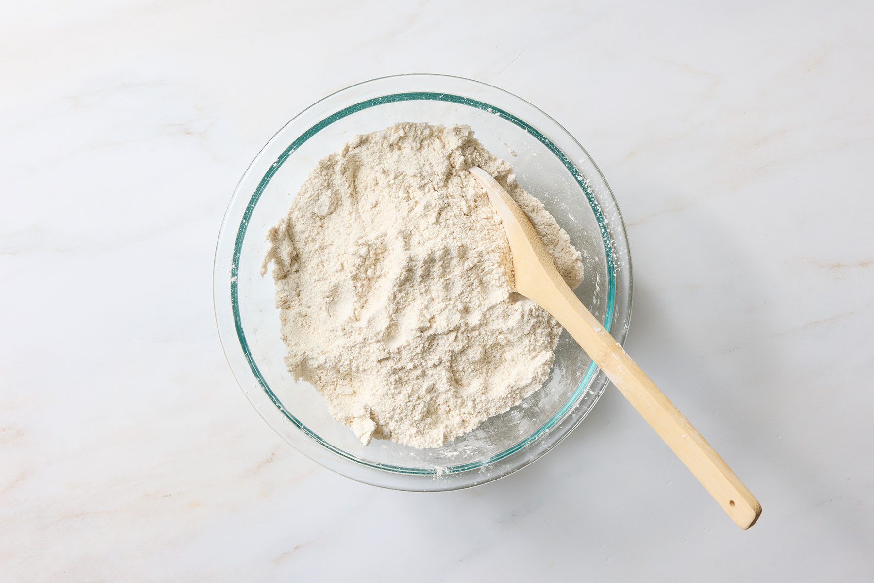 Combining flour, sugars, baking powder, salt, cinnamon, and nutmeg, whisking the ingredients together until they're well blended.