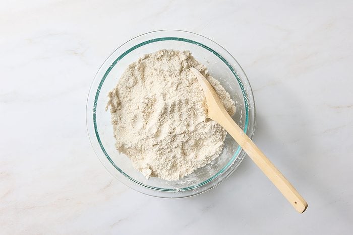 Combining flour, sugars, baking powder, salt, cinnamon, and nutmeg, whisking the ingredients together until they're well blended.