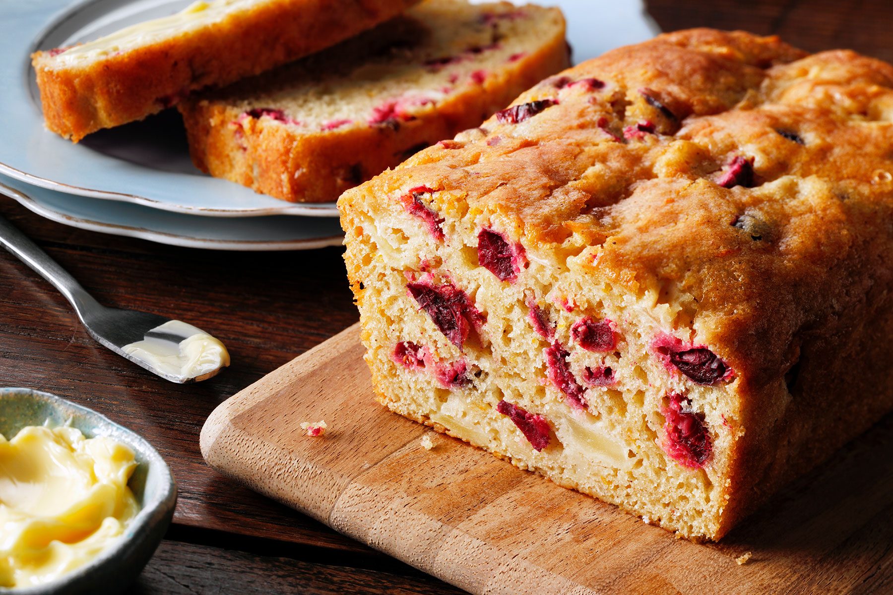 Cranberry Orange Bread load with pieces cut put on side and a small bowl of butter.