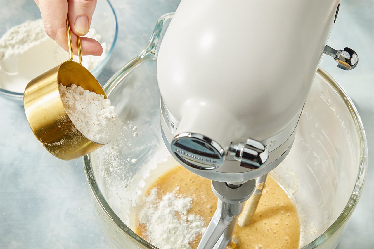 Overhead view of flour being added to the cookie dough mixture in a stand mixer, incorporating dry ingredients for marshmallow crispy cookies.