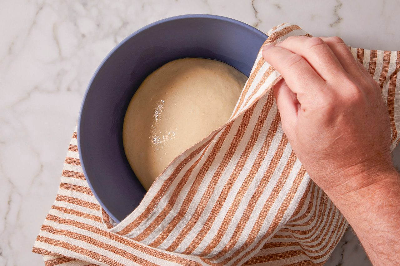 dough placed in a grease bowl covered with a cloth