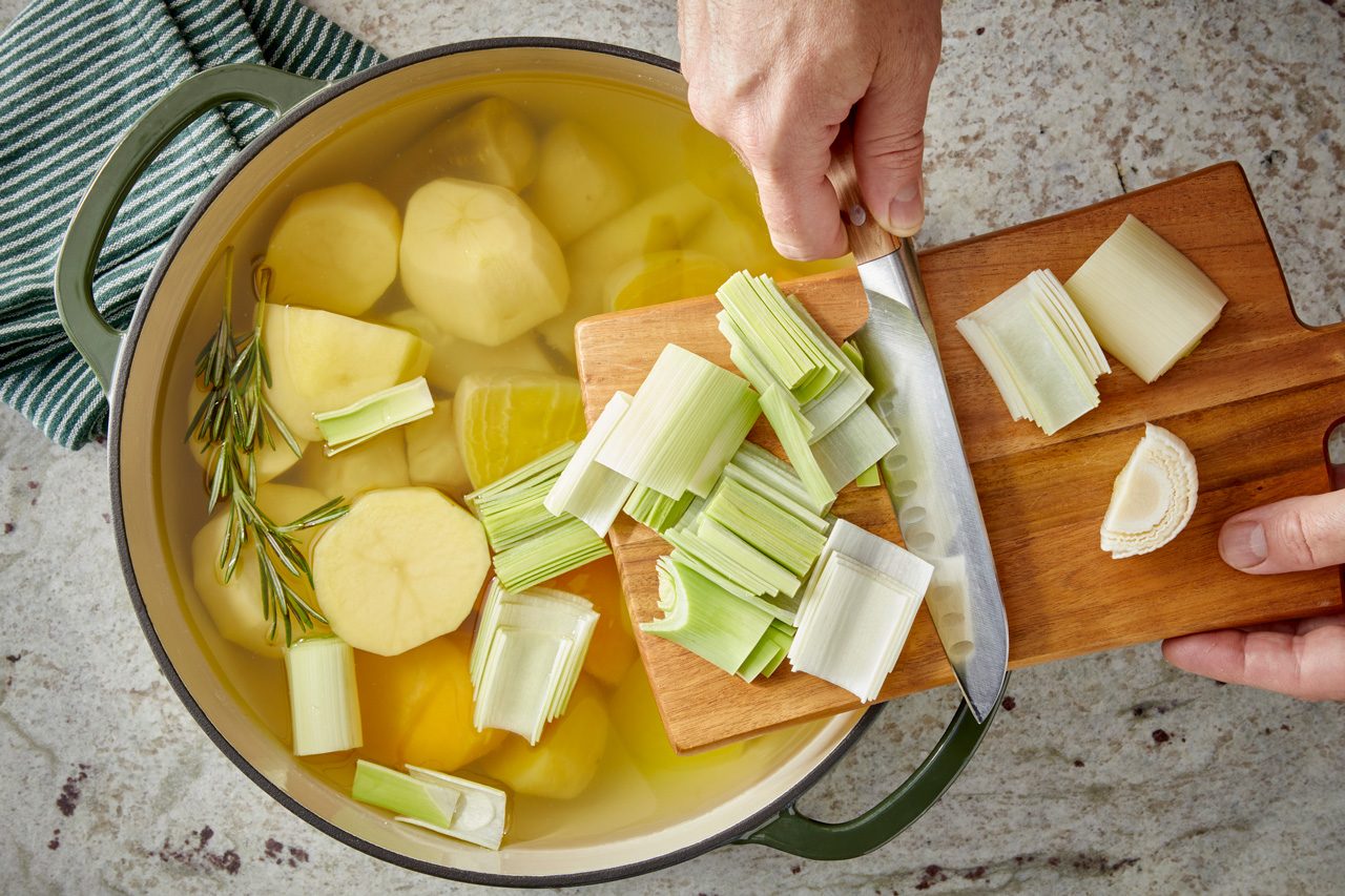chopped vegetables being added to water in a large dutch oven