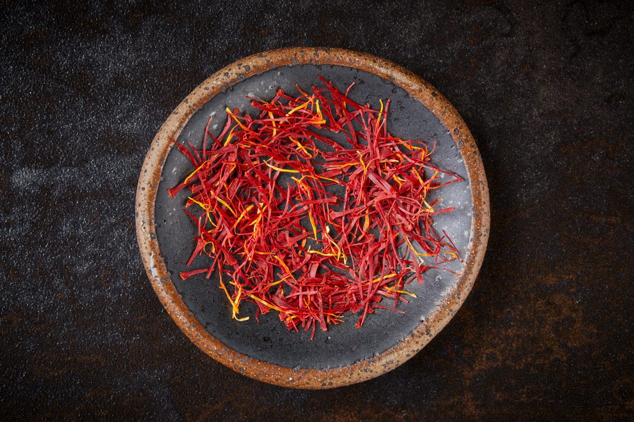 Overhead horizontal image of a dark grey ceramic plate filled with vibrant red and yellow saffron threads.