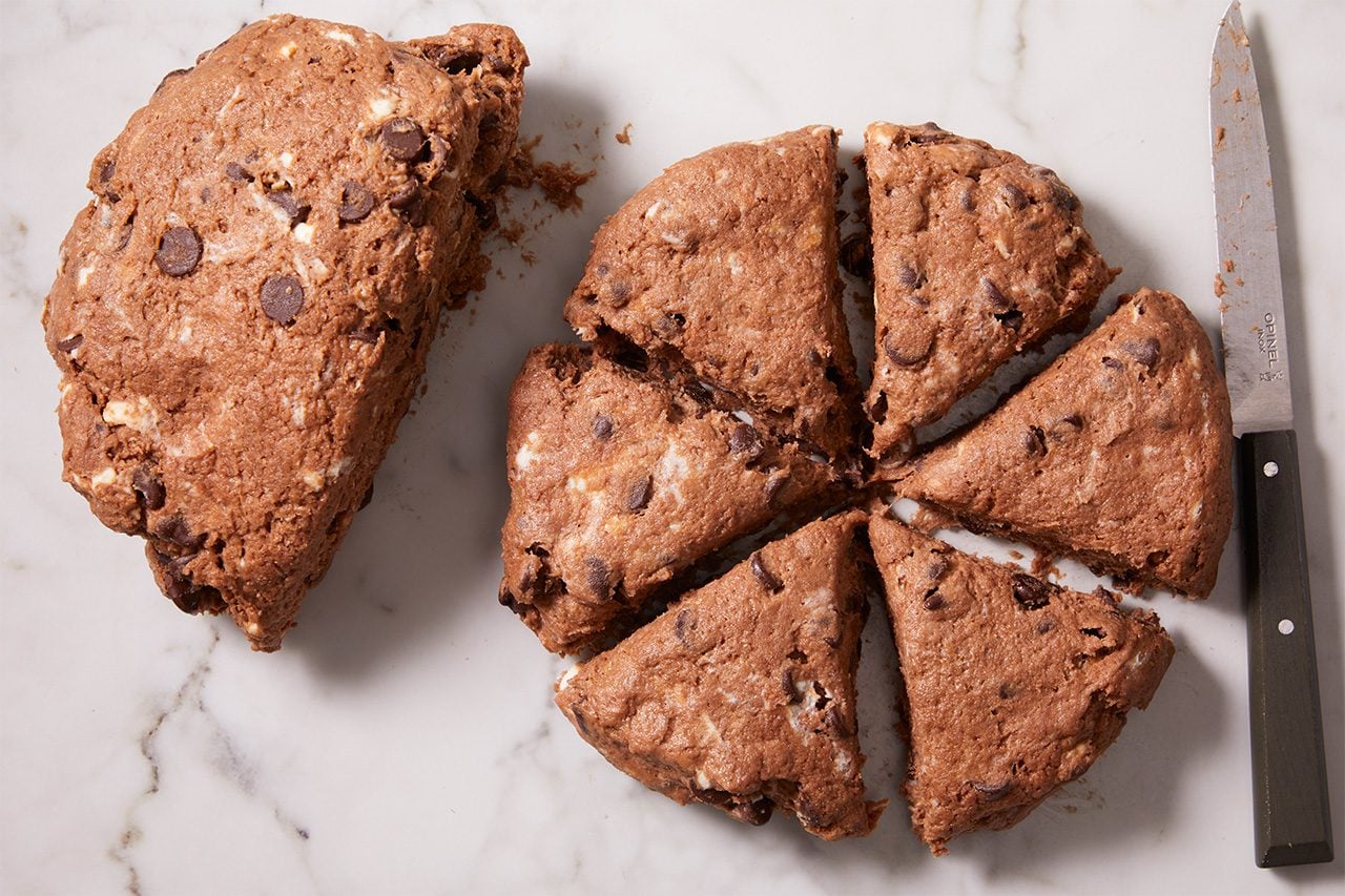 Chocolate chip scone round cut into six wedges on a marble surface, with one wedge separated and a knife placed beside the scone.
