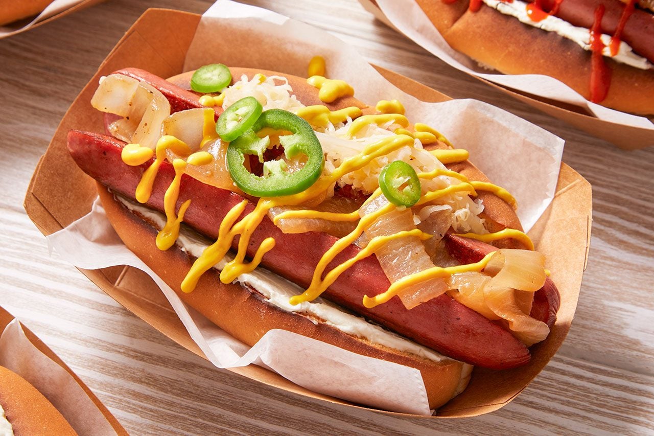 Close-up shot of a Seattle-style hot dog featuring a grilled sausage in a toasted bun, layered with cream cheese, caramelized onions, melted cheese, and topped with fresh jalapeño slices and a drizzle of mustard for a bold, flavorful finish.