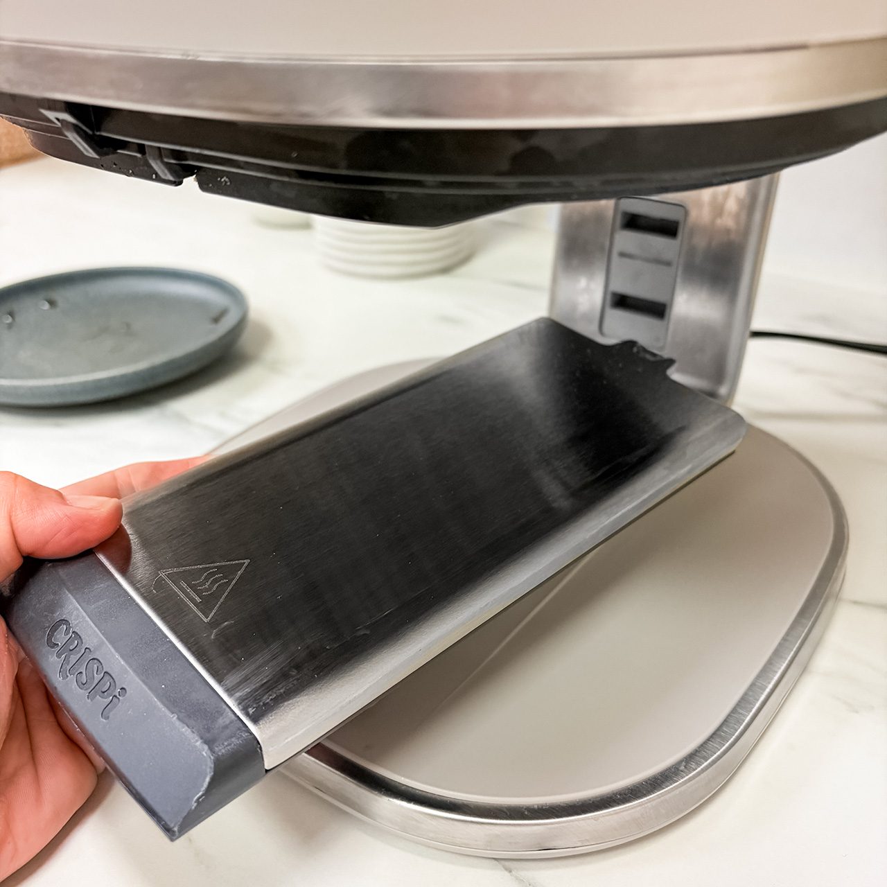A hand holds a Crisol chef’s knife sharpening guide against a metallic sharpening machine on a kitchen counter.