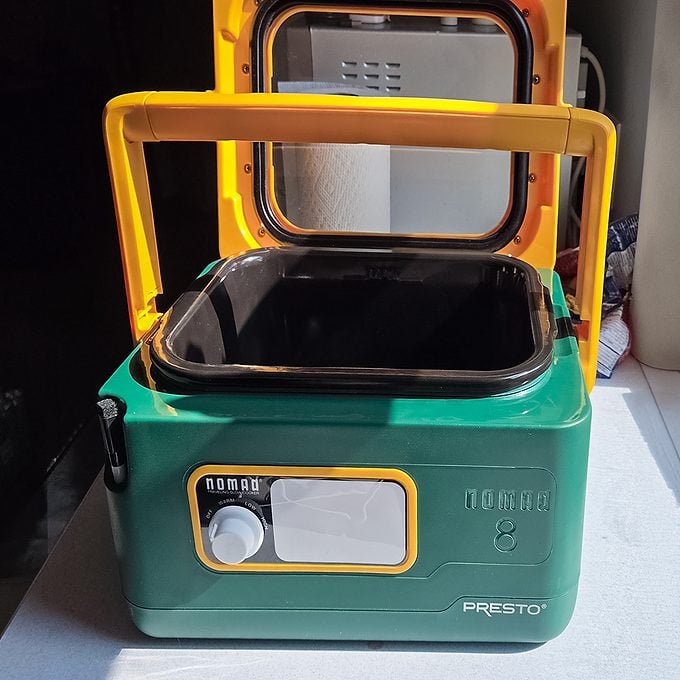 A green and yellow Presto Nomad portable slow cooker with an open lid, sitting on a counter in bright sunlight.