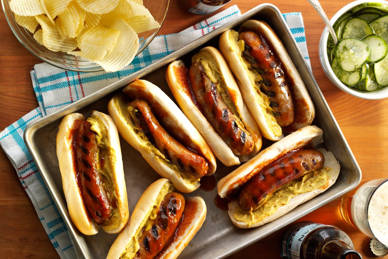 overhead shot of hot dogs on a table with chips and cucumbers in a bowl next to them