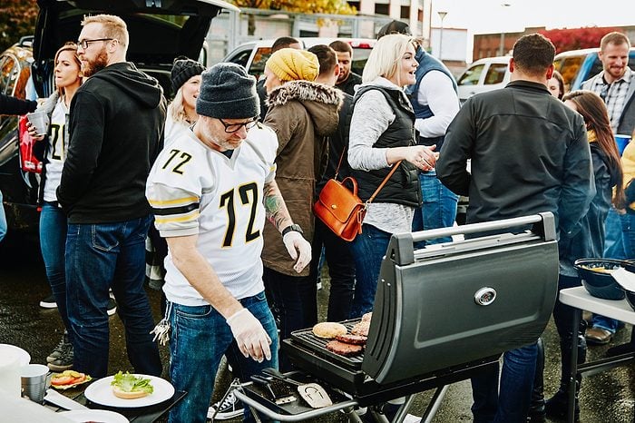 Man preparing food at barbecue for friends at tailgating party in stadium parking lot