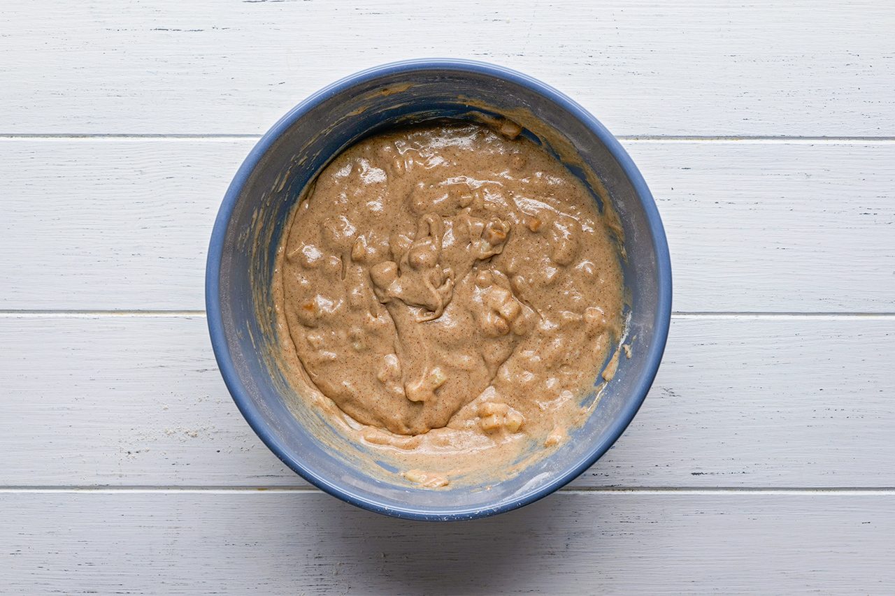 Blue bowl with lumpy, light brown batter on a white wooden surface, seen from above.
