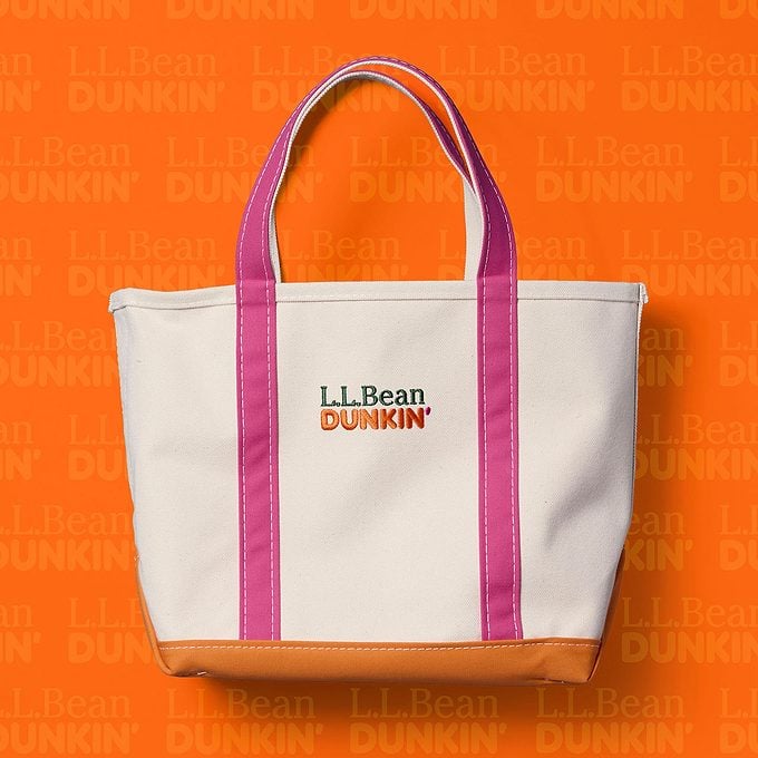 A white tote bag with pink handles and trim, orange bottom, and “L.L.Bean DUNKIN’” logo, set against an orange background