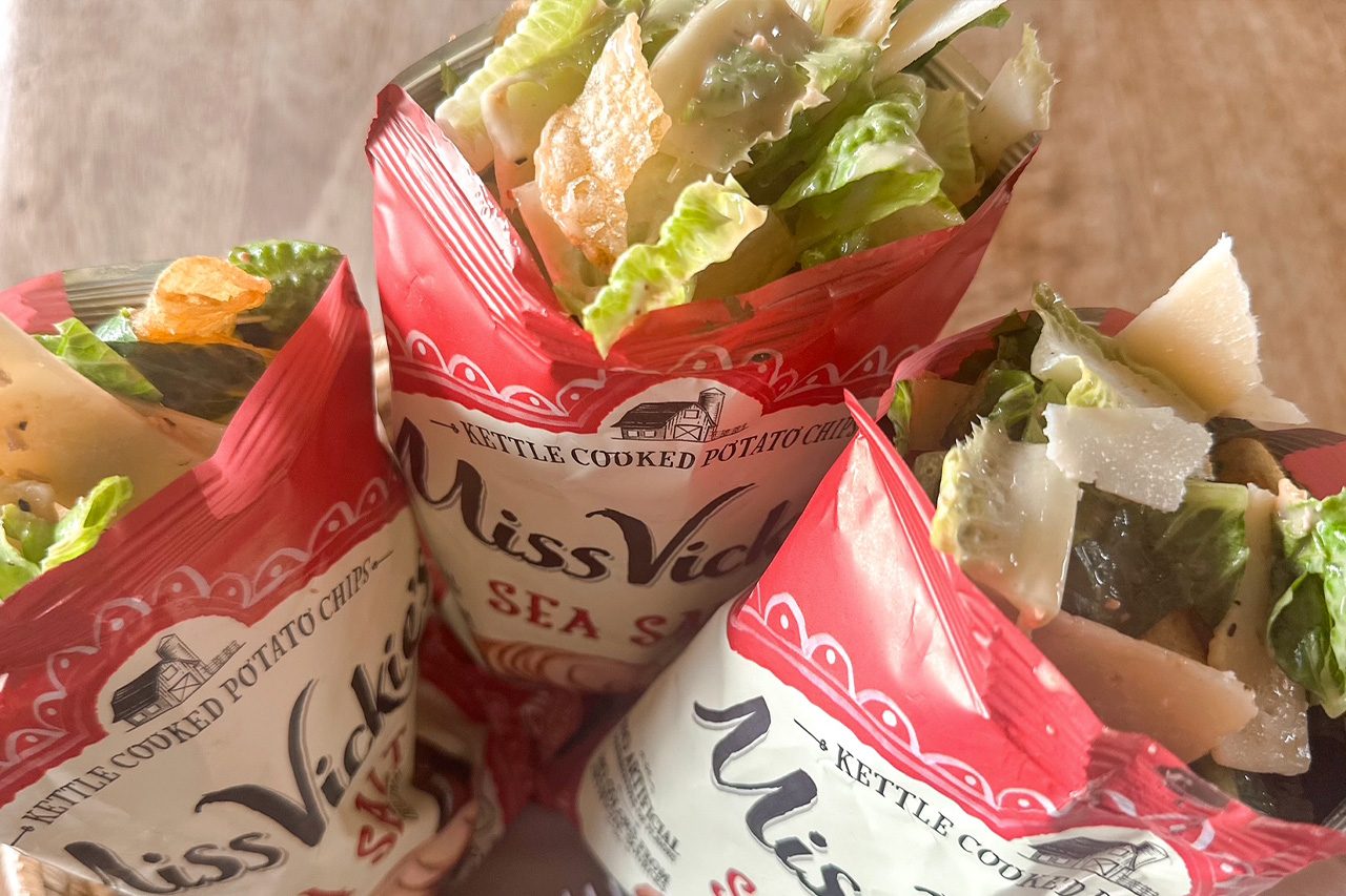 Three open red-and-white Miss Vickie’s Sea Salt kettle-cooked potato chip bags, filled with chips, lettuce, cheese, and salad ingredients.