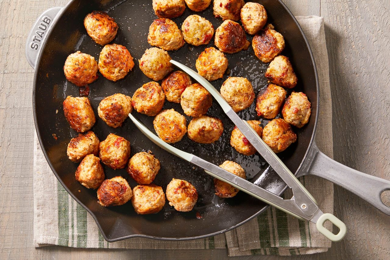 Overhead horizontal image of numerous browned meatballs in a black Staub cast iron skillet.