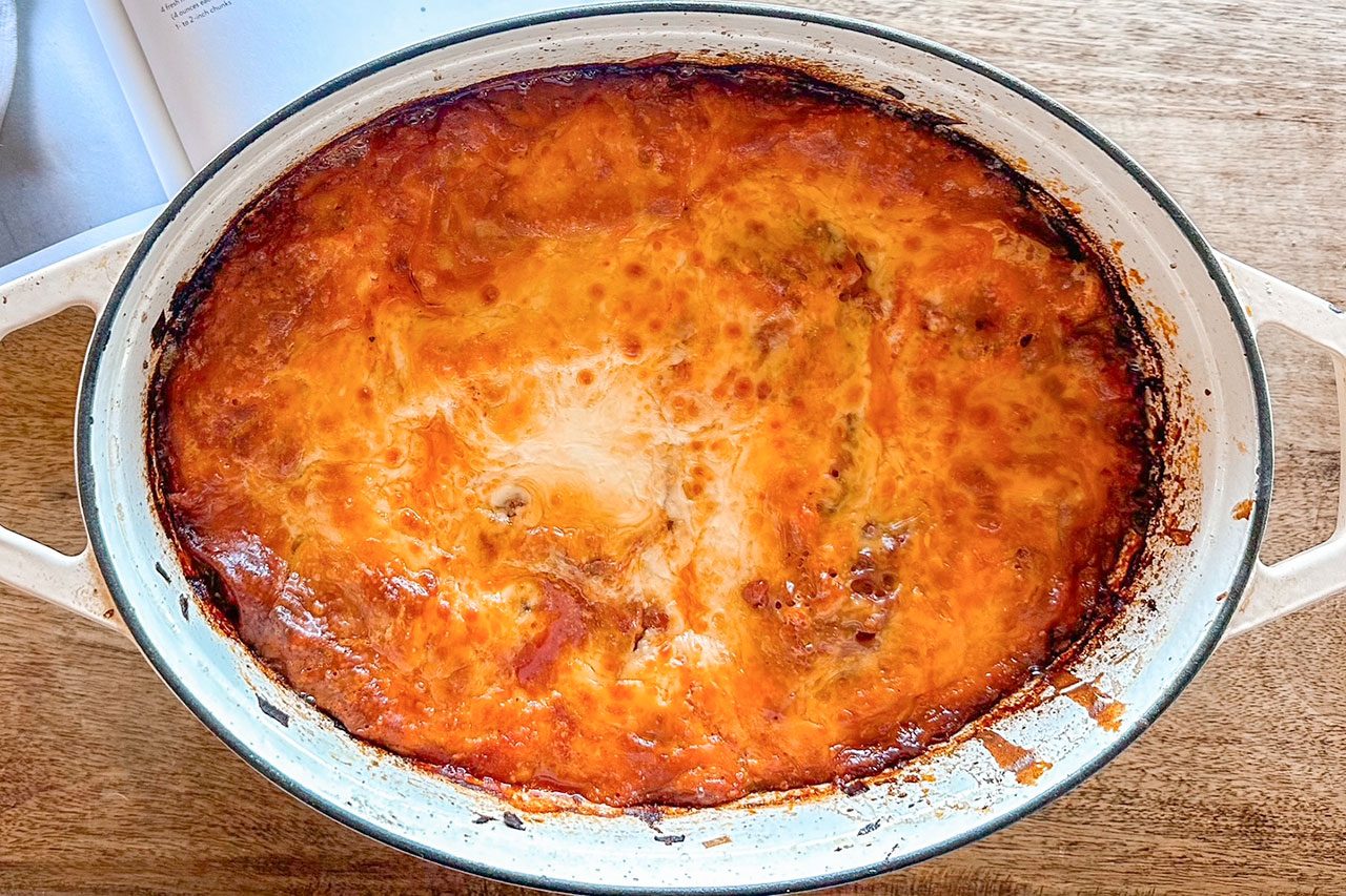 A baked dish with a golden-brown, slightly crispy top layer in a white oval casserole dish, sitting on a wooden surface.