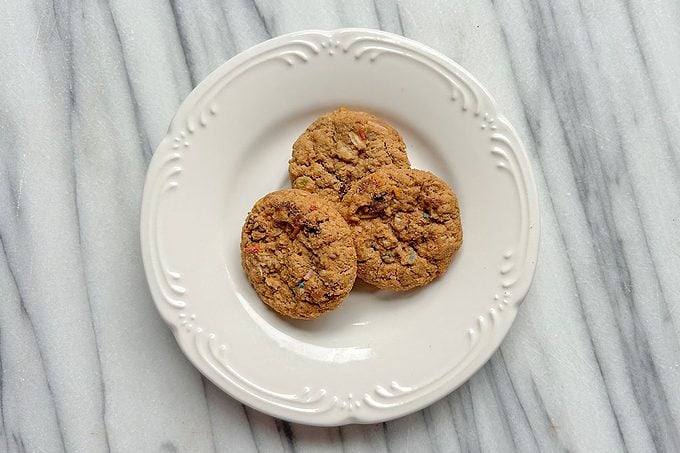 Three round, golden-brown cookies arranged on a white, decorative plate, set on a light gray marble surface.