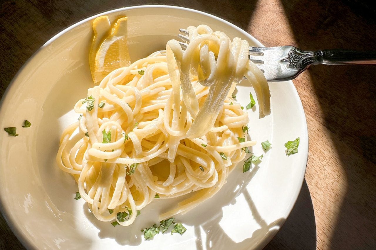 Sunlit plate of creamy spaghetti, with a fork lifting noodles, garnished with parsley and lemon; warm, inviting Italian meal.