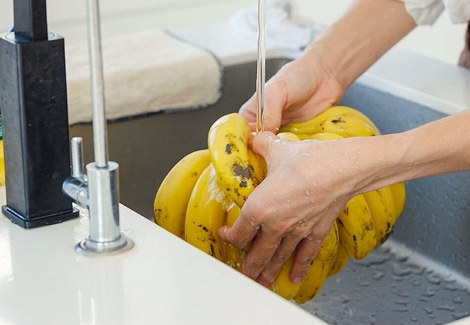 woman washing bananas in kitchen sink. home work in white modern kitchen